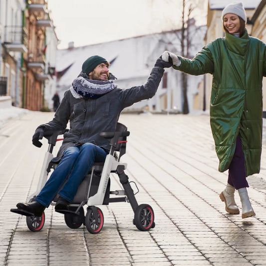 Mann fährt den Roamate elektrischen Rollstuhl im Winter auf einer Stadtstraße, Hand in Hand mit einer Frau – Freiheit und Mobilität im Alltag.