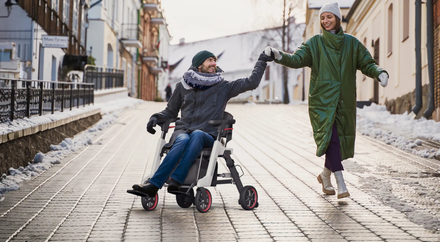 Mann fährt den Roamate elektrischen Rollstuhl im Winter auf einer Stadtstraße, Hand in Hand mit einer Frau – Freiheit und Mobilität im Alltag.