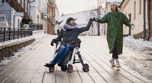Mann fährt den Roamate elektrischen Rollstuhl im Winter auf einer Stadtstraße, Hand in Hand mit einer Frau – Freiheit und Mobilität im Alltag.